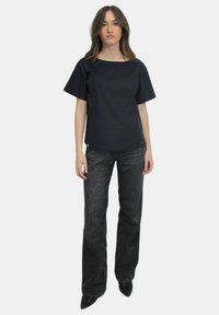 Top in cotone blu scuro a maniche corte con scollatura ampia, abbinato a jeans neri in denim a vita alta e a zeppe nere.