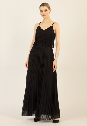 Zwarte plissé maxi-jurk met verstelbare spaghetti-bandjes, gelaagde ruffle bij de taille en een gladde textuur. Gemaakt met zwarte puntige schoenen.