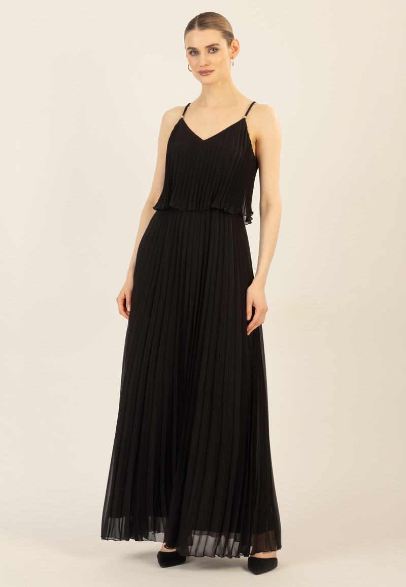 Zwarte plissé maxi-jurk met verstelbare spaghetti-bandjes, gelaagde ruffle bij de taille en een gladde textuur. Gemaakt met zwarte puntige schoenen.