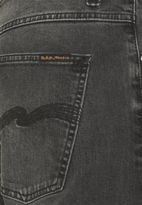 Černé džínové kalhoty s výrazným vlnitým švem na zadní kapse a oranžovou štítkem s nápisem "Hoodie Jeans Co."