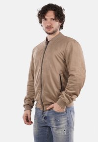 Giubbotto bomber in suede marrone con collo rotondo, chiusura con zip e tasche laterali. Morbido al tatto; polsini e vita aderenti; design casual.