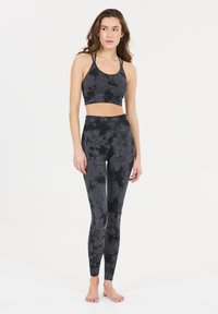 Ensemble de sport noir tie-dye comprenant un soutien-gorge et des leggings, fabriqué en tissu extensible. Présente un design court et des leggings taille haute avec une finition sans couture.