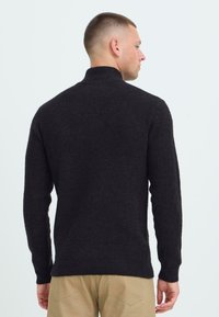 Dunkler Strickpullover mit hohem Kragen, langen Ärmeln und gerippter Struktur, von hinten betrachtet. Das Material wirkt weich und warm.