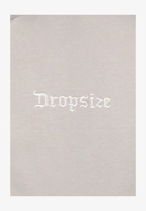 Helles graues Gewebe mit weicher Textur zeigt das Wort "Dropsize", das in weißer gotischer Schrift gestickt ist. Keine weiteren Muster oder Akzente.