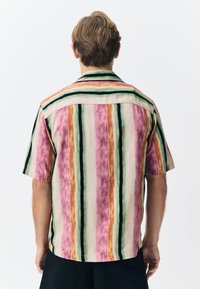 Chemise à manches courtes présentant des rayures verticales rose, orange, vert et noir, avec une coupe décontractée et un col classique. Tissu texturé.