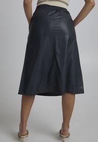 Jupe midi en cuir noir avec une taille élastique, texture lisse, forme évasée et ourlet au genou. Design minimaliste, sans motifs visibles.