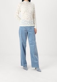 Spetsblus med långa ärmar i krämfärg, matchad med ljusblå kordbyxor med vida ben. Modell som bär ljusgrå spetsiga klackskor.