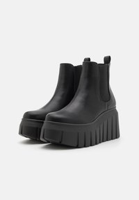 Stivaletti neri alla caviglia in pelle liscia con suola platform spessa caratterizzata da scanalature verticali e pannelli laterali elasticizzati per una facile calzata.