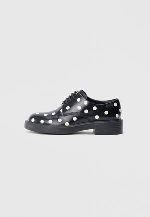 Black patent leather shoes with white polka dots, rounded toe, lace-up design, and a chunky black sole. Smooth texture, bold pattern.
