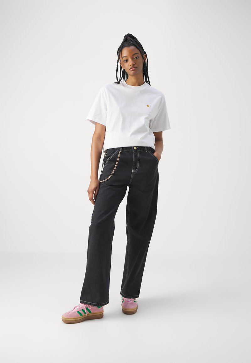 Hvid bomulds-T-shirt med et lille logo, parret med højtaljede sorte denimbukser med kædedetalje. Pink sneakers med grønne striber.