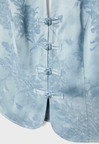Tissu bleu clair avec broderie florale et quatre fermetures nouées en forme de grenouille sur un vêtement traditionnel de style chinois.