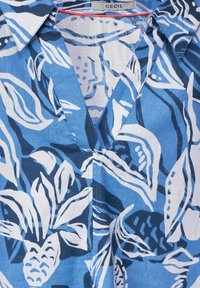 Blue patterned blouse with a V-neck, featuring leaves and floral designs in varying shades of blue and white, made of lightweight fabric.