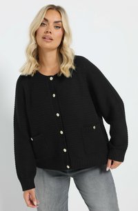 Svart stickad cardigan med stora knappar, ribbade ärmslut och två framfickor. Texturen är tjock och med en avslappnad passform.