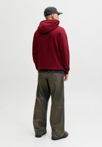 Bordeaux huppari rentoa istuvuutta, yhdistettyinä oliivinvihreisiin löysiin farkkuihin. Huomaamaton tekstuuri ja ompeluyksityiskohdat näkyvissä. Musta lakki päässä.