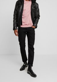 Svart läderjacka med dragkedjor, rosa T-shirt, svarta jeans och svarta chelsea boots. Avslappnad modern stil med en figurnära silhuett.