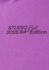 Tessuto di cotone viola caratterizzato da testo nero che recita "STUDIO Edizione Autunno 2025 (84°)". Texture liscia con sottili dettagli di cucitura.