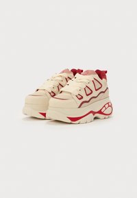 Zapatillas deportivas voluminosas con parte superior de tela beige, acentos rojos y suela de goma texturizada. Presentan puntera redondeada y cordones planos.