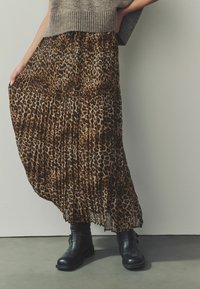 Maxi sukně s leopardím potiskem a sklady, vyrobená z lehkého materiálu, ve spojení s černými kotníkovými botami s akcentem pásku.