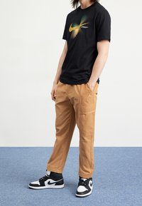 Svart t-shirt med färgglad Nike-logotyp, beige cargobyxor med fickor och en Jordan-logotyp, svartvita sneakers med en distinkt design.