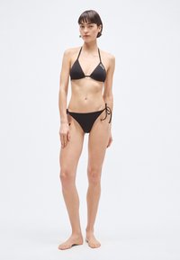 Čierny dvojdielny plavkový set s trojuholníkovým vrškom s tenkými ramienkami a zodpovedajúcim spodným dielom s viazačkami na bokoch, vyrobený z hladkej látky.