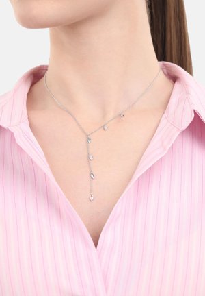 Collana d'argento con piccoli ciondoli a forma di foglia indossata al collo, abbinata a una camicia a righe rosa con colletto.