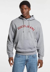 Felpa grigia con tasca frontale, con la scritta "GUESS JEANS" ricamata in rosso sul petto. Cappuccio regolabile con cordino, polsini a coste.