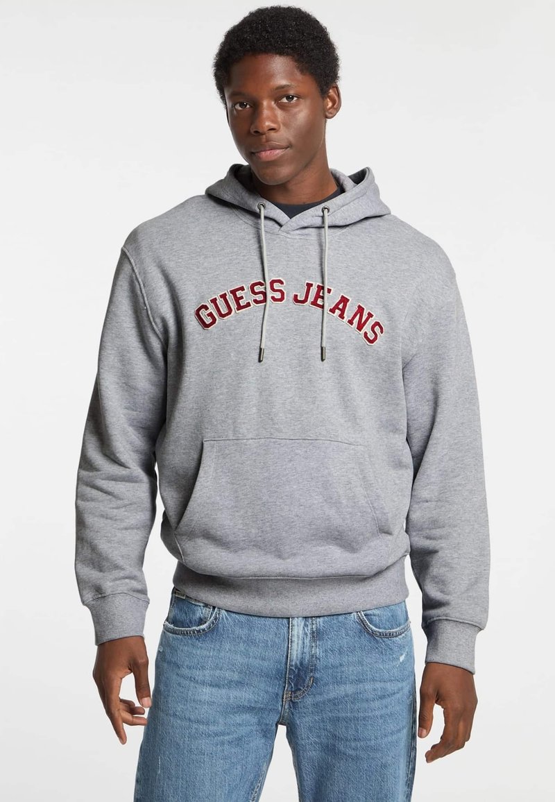 Felpa grigia con tasca frontale, con la scritta "GUESS JEANS" ricamata in rosso sul petto. Cappuccio regolabile con cordino, polsini a coste.