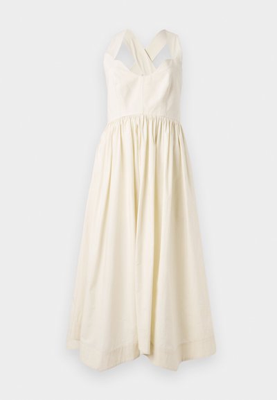 Abito di cotone color crema con un busto aderente e una gonna drappeggiata e fluida. Presenta spalline incrociate larghe e un design semplice.