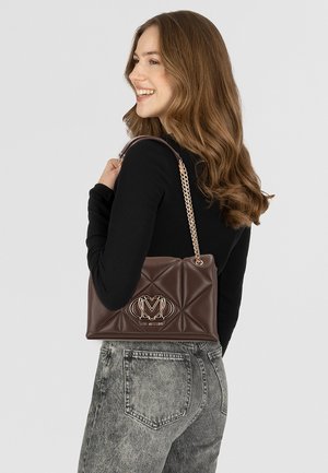 Borsa a tracolla in pelle marrone trapuntata con un accento del logo dorato, dotata di una tracolla a catena e una superficie testurizzata. Mostrata mentre viene tenuta sopra una maglia nera.