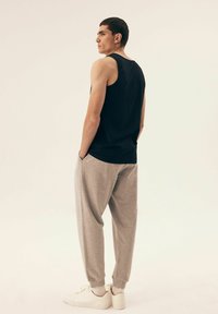 Black sleeveless tank top paired with light gray joggers. The joggers feature a relaxed fit and cuffed ankles, complemented by white sneakers.