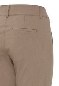 Gros plan sur l’arrière d’un pantalon habillé beige montrant un passant de ceinture, une ceinture et une poche passepoilée simple sans bouton visible.