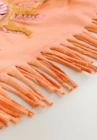Tissu orange avec franges le long du bord et un motif décoratif en perles dans des tons dorés et roses.