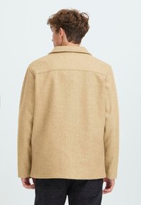 Brown, wool-blend jacket with a classic collar, relaxed shape, and long sleeves; features a smooth texture and simple stitching details.