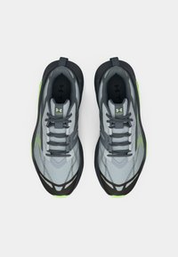 Ζεύγος γκρι και μαύρων αθλητικών παπουτσιών Under Armour με πράσινες λεπτομέρειες, ορατά από πάνω, που δείχνουν τα κορδόνια και τον επικαλυμμένο γιακά.