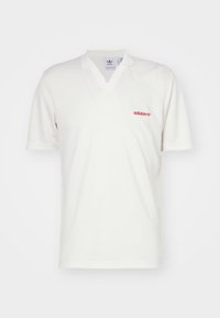 Bílá polo košile s výstřihem do V, krátkými rukávy a červeným logem Adidas na levé hrudi. Vyrobena z hladké, lehké tkaniny.