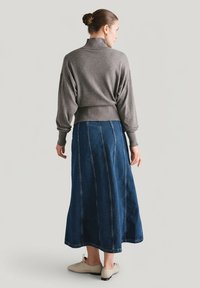 Szary, dzianinowy sweter z golfem w połączeniu z długą, ciemnoniebieską spódnicą jeansową z pionowymi szwami. Modelka ma na sobie jasnobeżowe buty.