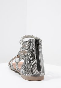 Harmaa ja musta käärmeennahkakuosisandaali, jossa on useita remmejä, teksturoitu yläosa ja takasaum zipper sulkemista varten. Littee pohja, jossa minimaalinen korkeus.