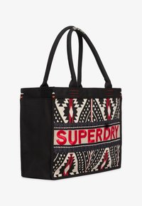Borsa a tracolla nera in tela con motivi geometrici ricamati e "SUPERDRY" in rosso. Presenta manici robusti e accenti in tessuto a contrasto.
