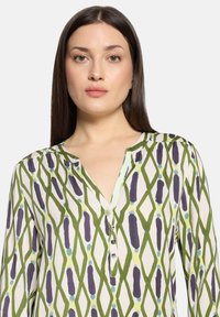 Bluzka z długim rękawem z lekkiego materiału z diamentowym wzorem w kolorach zielonym, fioletowym i niebieskim, z zapięciem na guziki przy dekolcie i luźnym krojem.
