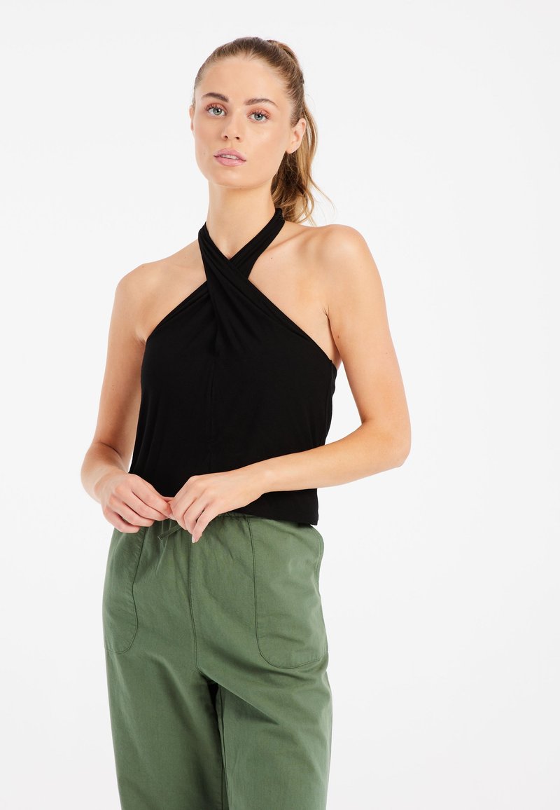 Top negro de tirantes con un diseño retorcido, hecho de tela suave. Combinado con pantalones sueltos de color verde claro que cuentan con dos bolsillos frontales.