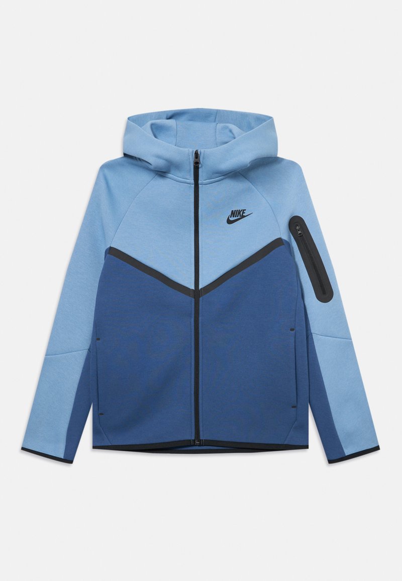 Nike bunda so striedavou kompozíciou v svetlom a tmavom modrom odtieni. Vyrobená z jemného materiálu, s vreckom na zips na rukáve a kapucňou.