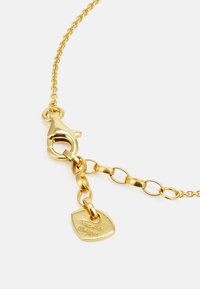 Pulsera de cadena en tono dorado con cierre de langosta, eslabones ovalados y una etiqueta en forma de corazón con detalles grabados.