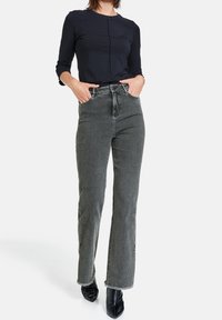 Top negro de manga larga con una costura central, combinado con jeans grises de tiro alto que presentan un dobladillo ligeramente deshilachado y bolsillos frontales.