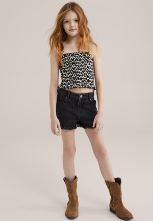 Fekete-fehér mintás crop top, amelyet rojtos fekete farmer rövidnadrággal és barna velúr cowboy csizmával párosítanak. Egyszerű dizájn, laza fazon.
