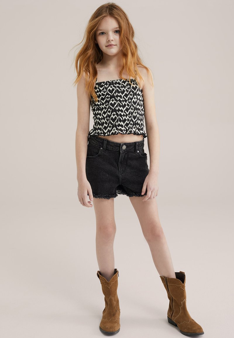Top corto de patrón en blanco y negro combinado con shorts de mezclilla negros deshilachados y botas de vaquero de ante marrón. Diseño sencillo, ajuste casual.