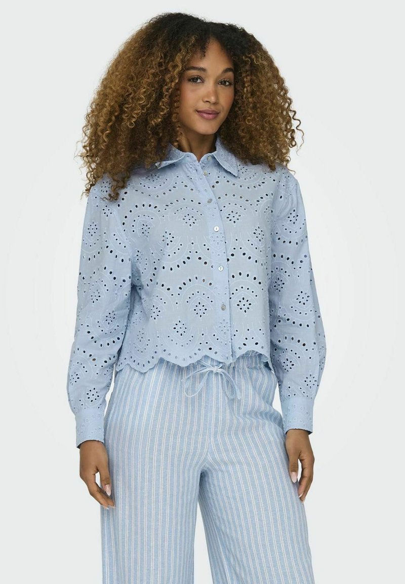 Camisa de botones azul claro con recortes de ojal, dobladillo con forma de scallop y mangas largas, combinada con pantalones con cordón de rayas claras.