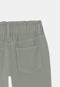 Light green pants featuring an elasticated waistband, back pocket with triangle logo, and textured fabric. Clean lines and tailored fit.