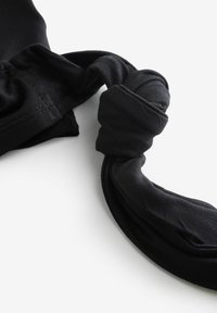 Melns auduma tops ar teksturētu materiālu, savītu siksnu detaļu un gludu virsmu ar izšūtām šuvēm.