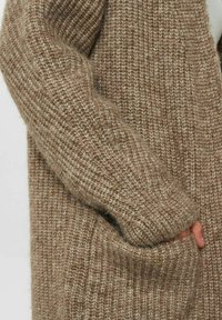 Stickad kofta i en ljusbrun nyans med ett strukturerat mönster, som har en lös passform, vida ärmar och djupa sidofickor.