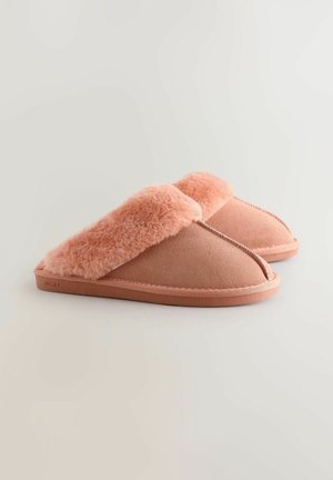 Chaussons rose clair avec un doux contrefort en fourrure duveteuse, en matière lisse semblable à du daim, et un design à bout rond. Présente un bord cousu et une semelle en caoutchouc.